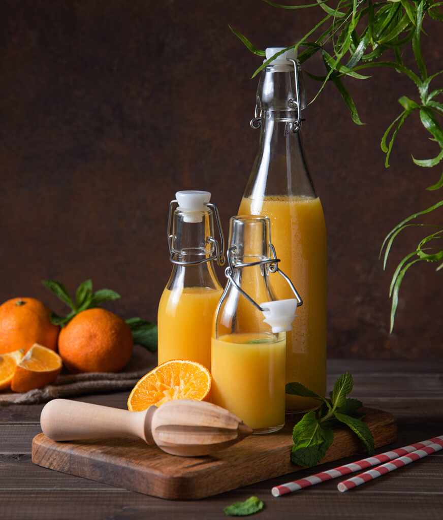 healthy-drink-concept-fresh-orange-juice-in-three-bottles-with-citrus-fruits-on-cutting-board-and-a-brown-wooden-background-front-view-and-dark